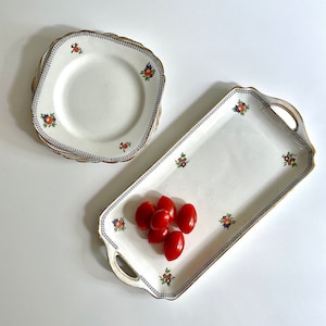 May include: A white ceramic serving tray with a floral design and gold trim. The tray is decorated with small red tomatoes.
