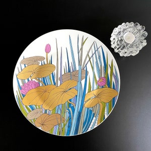 Puede incluir: Un plato de cer&aacute;mica blanco con un dise&ntilde;o floral azul, verde y rosa. El dise&ntilde;o presenta nen&uacute;fares y hojas estilizados.