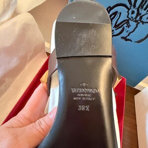 May include: Close-up of a brown leather sandal sole with gold-coloured studs. The brand name "Valentino Garavani" and "Made in Italy" are visible. The size is 38 1/2.