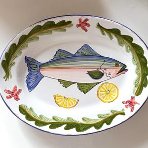 May include: Oval ceramic serving platter with a hand-painted fish design. The fish is blue, pink, and green, with a yellow lemon slice and red starfish accents. The rim is decorated with green seaweed and a blue border.