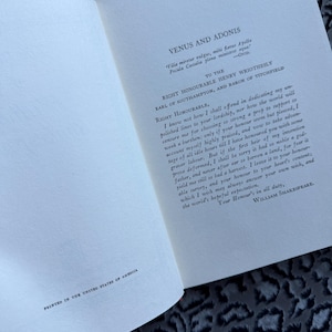 May include: Open book with text from "Venus and Adonis" by William Shakespeare. The text is printed in black ink on off-white paper. The phrase "Printed in the United States of America" is at the bottom.