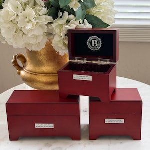 May include: Three dark cherry-colored wooden display boxes for coins. The top box is open, revealing a black interior with a circular logo featuring a B. Each box has a silver plaque reading The Complete NFL Silver Dollar Collection.