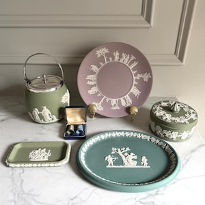 May include: Collection of antique ceramic pieces in shades of green and purple. Includes a teapot, a plate, a serving tray, a trinket box, and a small rectangular dish. Each piece features white bas-relief designs of classical figures.