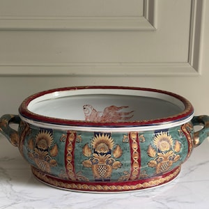 May include: Oval ceramic serving bowl with handles. The bowl features a teal background with gold floral and geometric patterns, red and gold trim, and a white interior with a fish illustration. The handles are teal and gold.