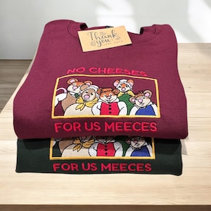 May include: Two sweatshirts, one burgundy and one dark green, are stacked. The burgundy sweatshirt has an embroidered design of cartoon mice with the text "NO CHEESES FOR US MEECEES." A small card with "Thank you very much" is on top.