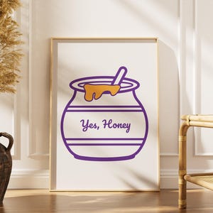 Może przedstawiać: Oprawiony wydruk z fioletową ilustracją słoika miodu z napisem "Yes, Honey". Słoik ma łyżkę i ociekający miód. Wydruk jest eksponowany w pokoju z wazonem z suszonymi roślinami i drewnianym stolikiem bocznym.
