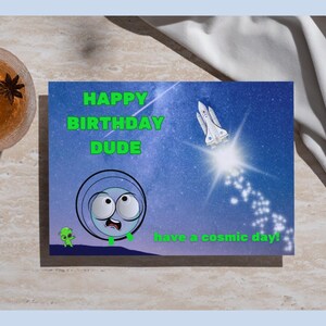 Peut inclure: Carte d'anniversaire sur le thème de l'espace. La carte présente un extraterrestre de dessin animé et une navette spatiale sur fond étoilé. Le texte sur la carte dit "HAPPY BIRTHDAY DUDE" et "have a cosmic day !" Un verre de liquide ambré avec de l'anis étoilé est dans le coin supérieur gauche.