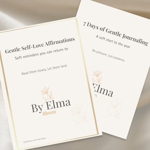 Op de afbeelding: Twee crèmekleurige kaarten met gouden randen en bloemaccenten. Eén kaart leest "Gentle Self-Love Affirmations", de andere "7 Days of Gentle Journaling". De tekst "By Elma Bloom" is ook zichtbaar. Een kleine theekopje staat op de achtergrond.