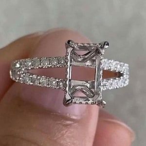 May include: A silver-toned ring featuring a rectangular prong setting designed for a center stone. The band is split into two sections, both encrusted with small, clear pavé-set stones that extend along the sides of the ring's shank.