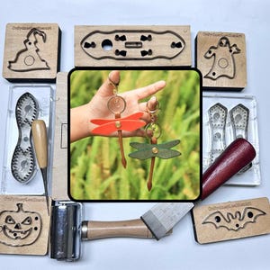 May include: A collection of leather crafting tools and accessories. Includes wooden stamps with Halloween designs, a mallet, and two dragonfly keyrings in orange and green. The keyrings are held in a hand.