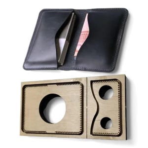 May include: Black leather wallet, open to show a phone and banknotes, above a wooden die-cut template. The wallet has card slots and a bill compartment. The template features a large circular cutout and smaller shaped cutouts.