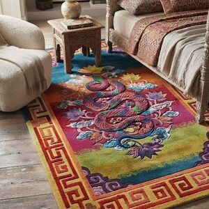 Könnte beinhalten: Ein rechteckiger Teppich mit einem zentralen, gewundenen Drachenmotiv, umgeben von Lotusblumen in leuchtenden Rosa-, Orange-, Blau- und Grüntönen. Der Teppich hat eine markante rote geometrische Mäanderbordüre und den Text RUG MAGAZINE in der Ecke.