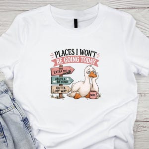 May include: A white t-shirt featuring a graphic of a tired white duck holding a pink mug labeled NOPE. Next to the duck is a wooden signpost with three signs reading THE EXTRA MILE, ABOVE & BEYOND, and OUTTA MY WAY, with the text PLACES I WON'T BE GOING TODAY.