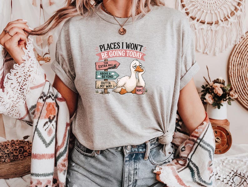 May include: A heather gray t-shirt featuring a graphic of a tired white duck holding a pink mug labeled NOPE. The text reads PLACES I WON'T BE GOING TODAY above three directional signs pointing to THE EXTRA MILE, ABOVE & BEYOND, and OUTTA MY WAY.