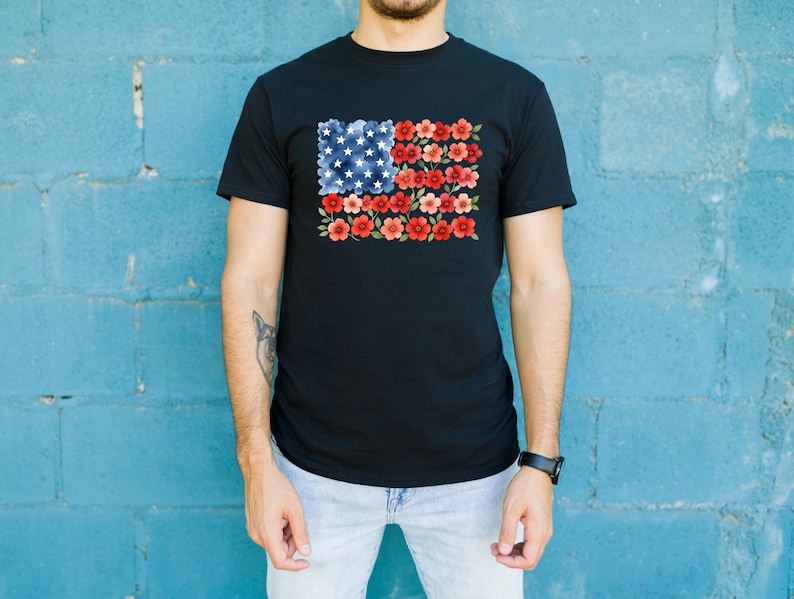 May include: Black t-shirt featuring a floral American flag design. The flag's stars are represented by white flowers on a blue background, and the stripes are red flowers. The shirt is a classic crew neck style.
