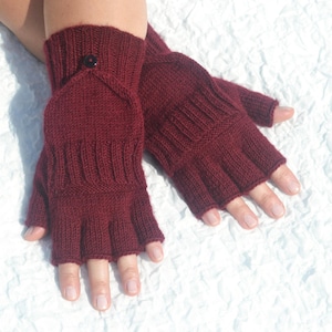 Op de afbeelding: Bordeauxkleurige vingerloze handschoenen met een knoopsluiting. Deze gebreide handschoenen hebben een geribbeld ontwerp en bedekken de vingers tot aan de knokkels. De handschoenen worden getoond op een wit, getextureerd oppervlak.