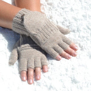 Może przedstawiać: Para beżowych rękawiczek bez palców wykonanych z dzianiny wełnianej. Rękawiczki są noszone na dłoniach osoby, z odsłoniętymi palcami.