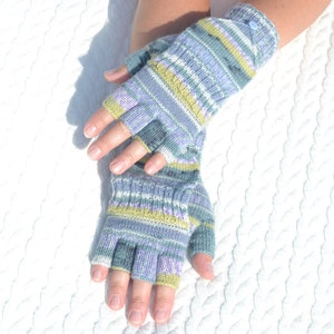 Könnte beinhalten: Ein Paar Fingerlose Handschuhe mit einem gestreiften Muster in Blautönen, Lila und Grün. Die Handschuhe sind aus weichem, gestricktem Stoff.
