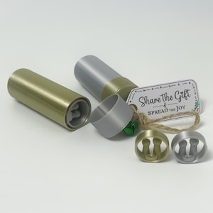 May include: A set of metallic bottle stoppers and a cylindrical container. The stoppers are in gold and silver, with a matching container in gold. A tag with the text "Share the Gift & Spread the Joy" is attached.