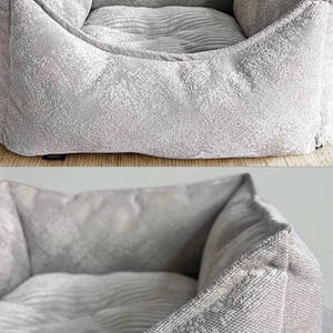 May include: A light gray dog bed with a textured, patterned fabric. The bed has a square shape with raised sides and a cushioned interior. The fabric appears soft and comfortable, suitable for a pet to rest in.