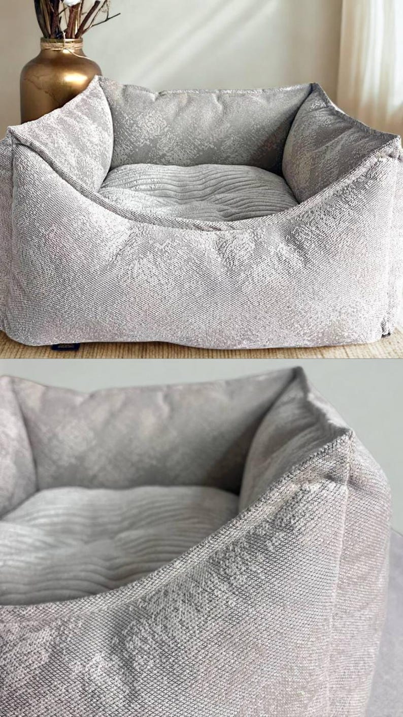 May include: A light gray dog bed with a textured, patterned fabric. The bed has a square shape with raised sides and a cushioned interior. The fabric appears soft and comfortable, suitable for a pet to rest in.