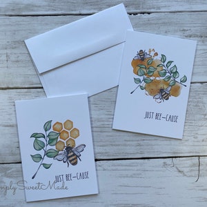 May include: Two greeting cards with a bee and honeycomb design. The text on the cards reads "Just Bee-Cause".