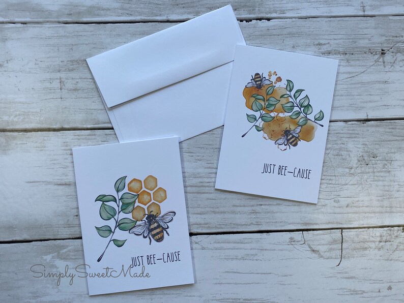May include: Two greeting cards with a bee and honeycomb design. The text on the cards reads "Just Bee-Cause".