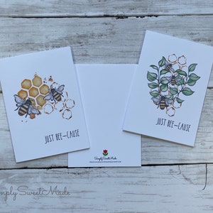 May include: Two greeting cards with bee illustrations and the text "Just Bee-Cause". One card features bees on a honeycomb with a watercolor effect. The other card features bees on a branch with green leaves.