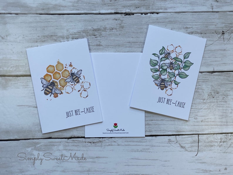 May include: Two greeting cards with bee illustrations and the text "Just Bee-Cause". One card features bees on a honeycomb with a watercolor effect. The other card features bees on a branch with green leaves.