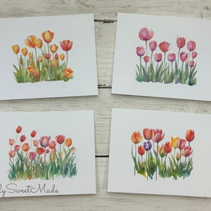 May include: Four greeting cards with watercolor paintings of tulips in various colors, including orange, red, and pink. The tulips are depicted with green stems and leaves, set against a white background.