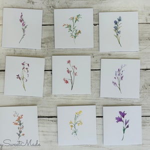 May include: Nine watercolor floral illustrations on white cards. The flowers are painted in shades of purple, blue, pink, red, yellow, and green.
