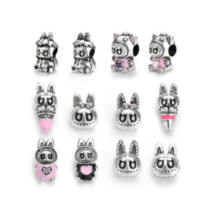 Könnte beinhalten: Eine Sammlung von silberfarbenen Charm-Anhängern mit verschiedenen Tierdesigns. Die Charms zeigen Hasen- und Katzenfiguren mit rosa und schwarzen Akzenten. Einige Charms haben ein rosa oder schwarzes Herzmotiv.