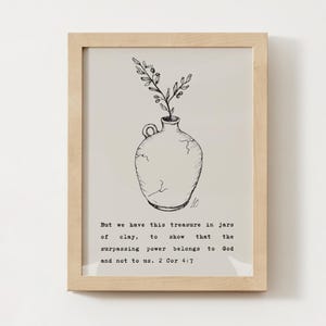 May include: A framed art print featuring a hand-drawn illustration of a vase with a sprig of leaves. The vase is cracked and has a handle. The print includes the text "But we have this treasure in jars of clay, to show that the surpassing power belongs to God and not to us. 2 Cor 4:7."