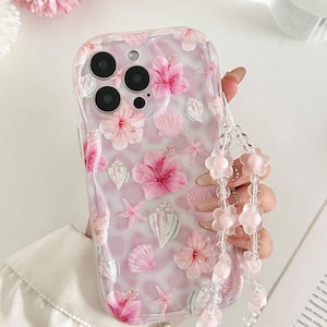 May include: A clear phone case decorated with pink hibiscus flowers, seashells, and starfish. The case has a beaded strap with pink flower-shaped beads. The design is a mix of floral and marine elements.