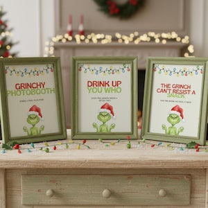 May include: Three framed prints with green frames and festive text and illustrations. The prints feature the Grinch in a Santa hat with phrases like "Grinchy Photobooth" and "Drink Up You Who". Colourful string lights decorate the top of each frame.