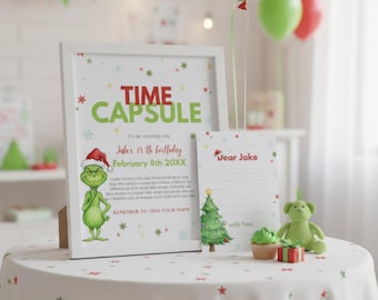 Puede incluir: Una impresión enmarcada de "Time Capsule" con una ilustración del Grinch, una carta y un pequeño oso de peluche verde sobre una mesa. La impresión incluye el texto "15 cumpleaños de Jake, 8 de febrero de 20XX". Una magdalena y una pequeña caja de regalo también están sobre la mesa.