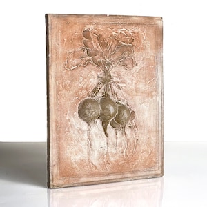 May include: A rectangular, textured wall plaque featuring a relief of a bunch of radishes. The radishes are depicted with their leaves and roots, tied together. The plaque has a light brown background with white accents.