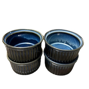 Puede incluir: Cuatro ramequines de cerámica azul oscuro con exterior acanalado e interior azul brillante. Los ramequines están apilados en pares, mostrando su forma redonda y colores contrastantes. Ideal para hornear y servir porciones individuales.