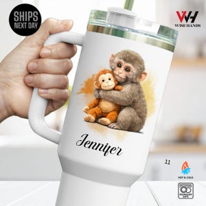 May include: White travel mug featuring a watercolor illustration of two monkeys hugging. The mug has a white handle and a clear lid. The name "Jennifer" is written in cursive below the illustration. The mug is dishwasher safe and suitable for hot and cold beverages.