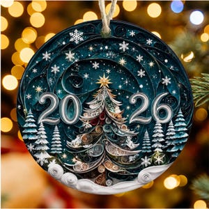 May include: A round Christmas ornament featuring a quilled paper-style design of a central tree, the year 2026, and smaller pine trees against a dark blue background with white snowflakes and a star topper, suspended by a light-colored string.