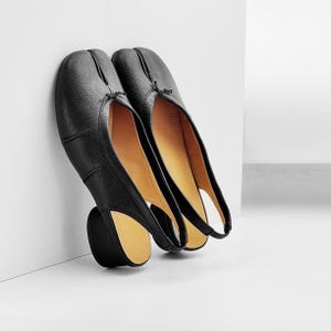 May include: A pair of black split-toe ballet flats with a low heel. The shoes are made of smooth leather and have a distinctive design with a split between the big toe and the other toes. The interior is a light tan color.