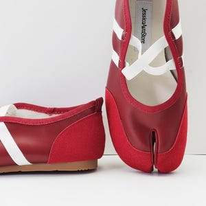 Puede incluir: Bailarinas rojas y blancas con puntera dividida, puntera de ante y correas blancas. Los zapatos tienen un tac&oacute;n bajo y una suela marr&oacute;n. El nombre de la marca "JessicaAuraStore" est&aacute; impreso en la plantilla.