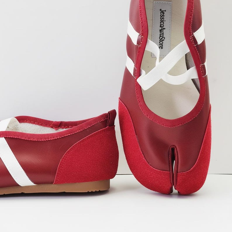Puede incluir: Bailarinas rojas y blancas con puntera dividida, puntera de ante y correas blancas. Los zapatos tienen un tac&oacute;n bajo y una suela marr&oacute;n. El nombre de la marca "JessicaAuraStore" est&aacute; impreso en la plantilla.