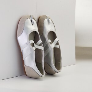 Puede incluir: Un par de zapatos plateados y beige con puntera dividida y una correa en la parte superior. Los zapatos tienen un dise&ntilde;o &uacute;nico con una divisi&oacute;n entre el dedo gordo y los otros dedos. Las suelas son marrones.