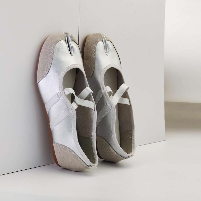Puede incluir: Un par de zapatos plateados y beige con puntera dividida y una correa en la parte superior. Los zapatos tienen un dise&ntilde;o &uacute;nico con una divisi&oacute;n entre el dedo gordo y los otros dedos. Las suelas son marrones.