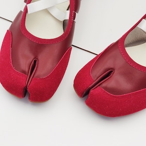 Puede incluir: Par de zapatos rojos con puntera dividida y correas blancas. Los zapatos presentan un dise&ntilde;o &uacute;nico con un compartimento separado para el dedo gordo y est&aacute;n hechos de cuero y ante. Los zapatos est&aacute;n dise&ntilde;ados para la comodidad y la flexibilidad.