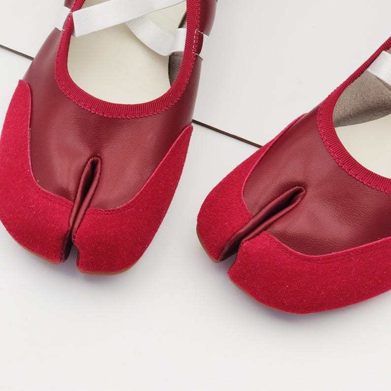 Puede incluir: Par de zapatos rojos con puntera dividida y correas blancas. Los zapatos presentan un dise&ntilde;o &uacute;nico con un compartimento separado para el dedo gordo y est&aacute;n hechos de cuero y ante. Los zapatos est&aacute;n dise&ntilde;ados para la comodidad y la flexibilidad.