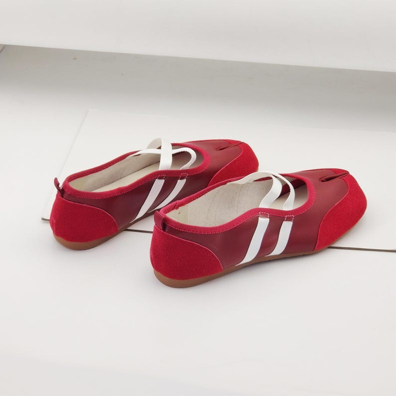 Puede incluir: Un par de bailarinas rojas con detalles blancos. Los zapatos tienen un dise&ntilde;o de puntera dividida y correas blancas. Las bailarinas presentan una puntera y un tal&oacute;n de ante rojo, con dos rayas blancas en el lateral.