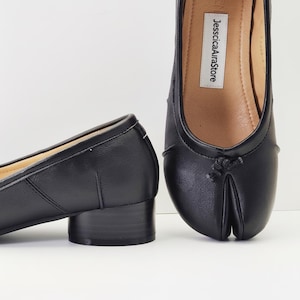 Op de afbeelding: Zwarte leren schoenen met split-teen en een lage blokhak. De schoenen hebben een ronde neus en een klein strikdetail. De binnenzool is beige met de tekst "JesscicaAiraStore".