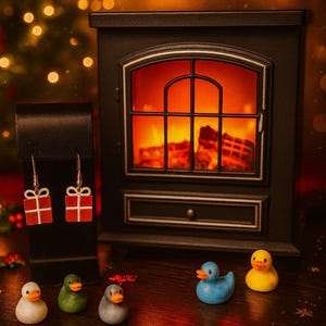 May include: A festive scene featuring Christmas-themed earrings shaped like red gift boxes, displayed on a black stand. Miniature rubber ducks in various colors are arranged in front of a fireplace, with a Christmas tree in the background.
